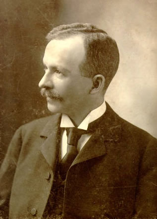 Sepia photograph of Charles Chesnutt. He is facing left. He has a moustache and short hair. He is wearing a suit.