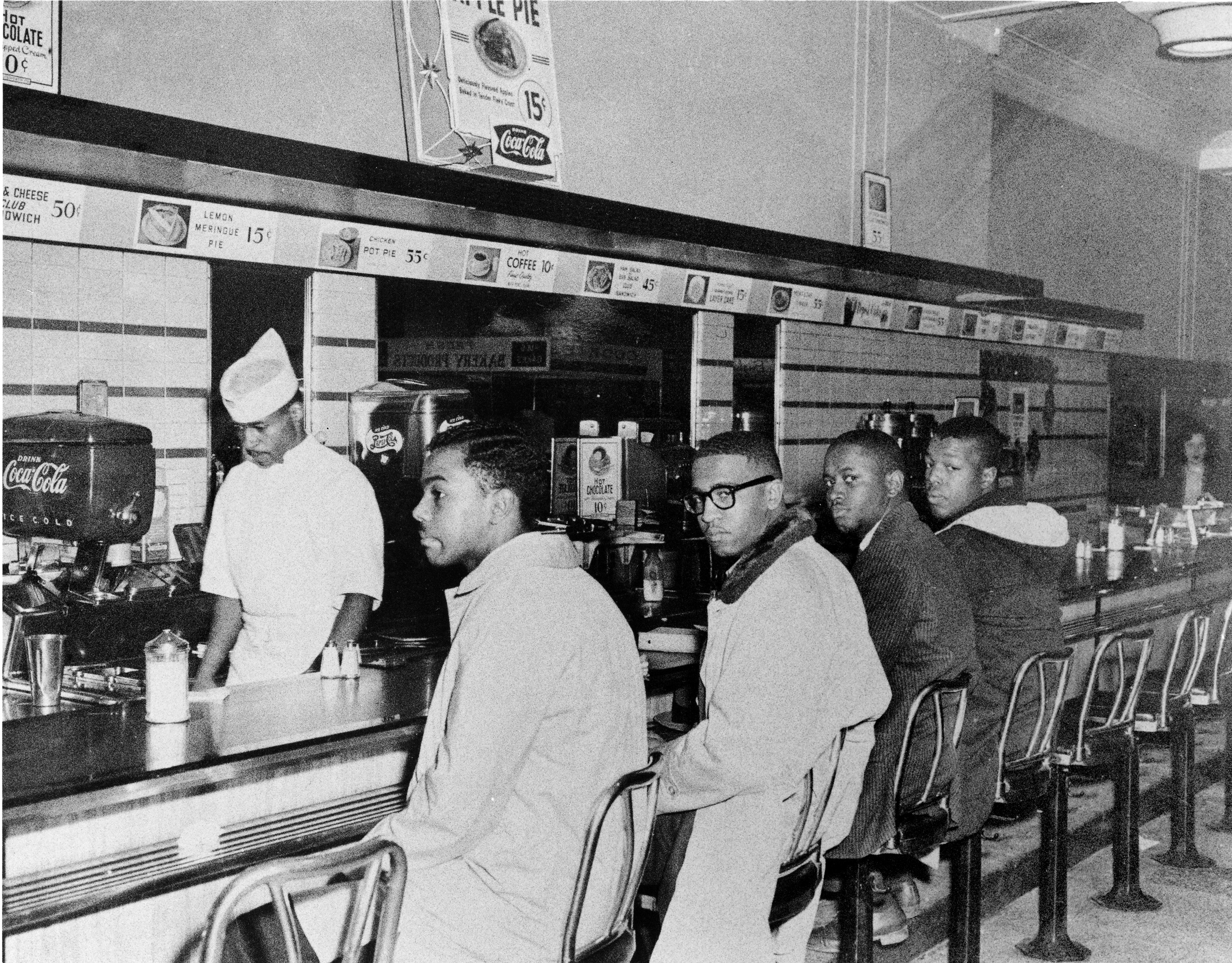 This is a historical photograph of four male African American students sitting at the counter of Woolworth in Greensboro, North Carolina, 1960.