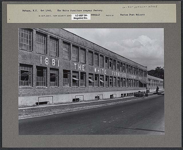 Black and white photograph of the White Furniture Company Factory. Many windows and a brick face present the building.
