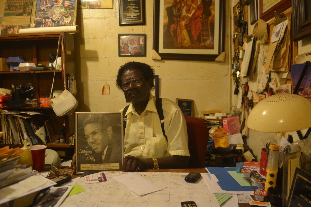 Photograph of Bennie R. Rountree at his desk holding a framed image of Golden Frinks. Photo taken by Steven A. Hill, July 28, 2018. Image used by permission.