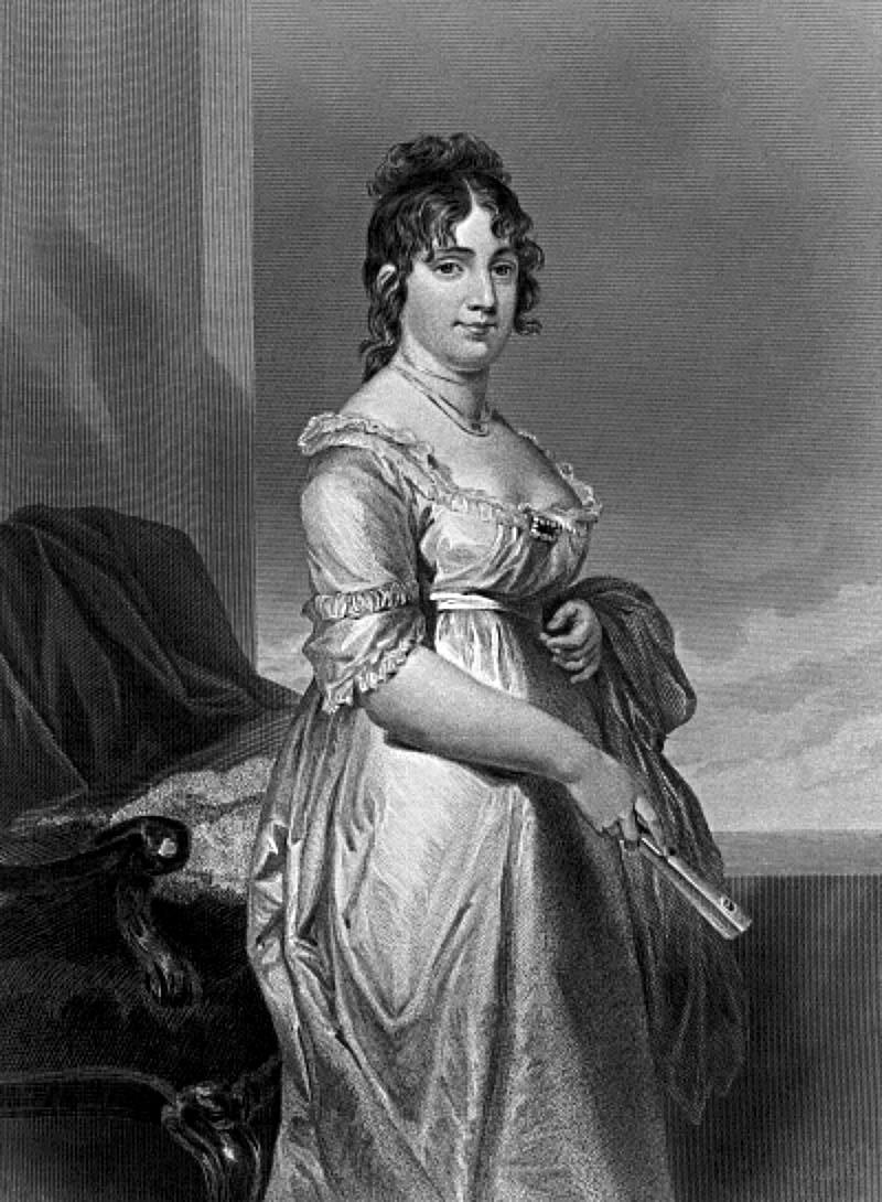 Dolley Madison Dolley Madison. Black and white. She is standing beside an armchair wearing a light dress with her hair up. She is holding a hand fan.
