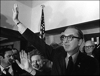 Jesse Helms celebrates his victory, 1972 Jesse Helms celebrating his victory. He is pictured waving to a crowd. He has glasses, a suit, slicked hair, and no facial hair. He has a triumphant expression.