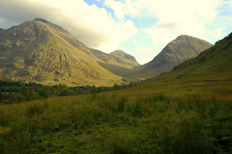 Scottish Highlands Scottish Highlands. Rolling green hills with mountains in the background. The sky is cloudy but blue.