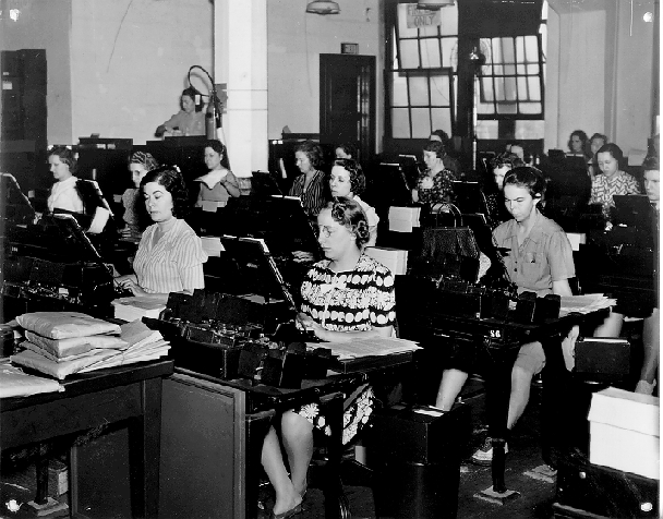 Several women, punch card operators, sit in an office and perform their work.