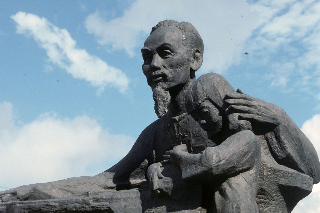 A statue of Ho Chi Minh. He has a long, thin beard. He is hugging a child.