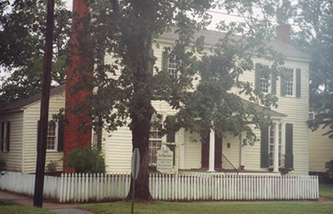 The Asa Biggs House. Trees obscure the foreground but a white, two-story home sits in the background.