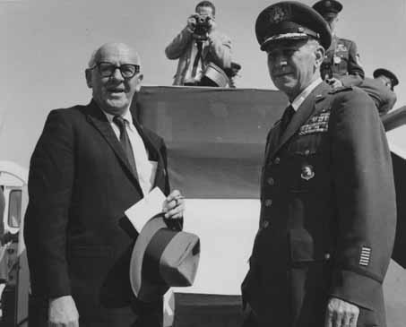 General Frank A. Armstrong, Jr. and an unidentified man standing together during Eisenhower's visit to Elmendorf Air Force Base in Anchorage, Alaska. Photographer and other military officers behind them. 